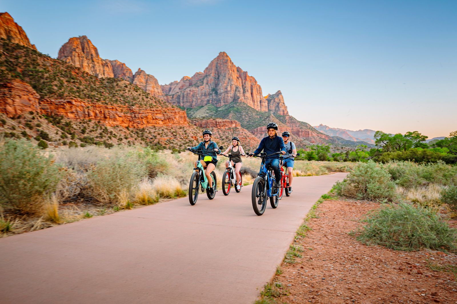Family biking along Pa'rus Trail in Zion National Park with stunning red rock canyon formations and desert landscape views