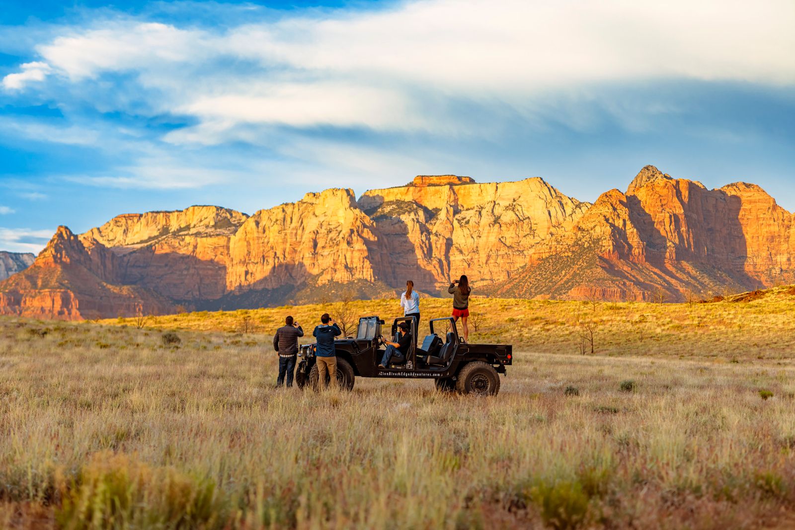 Tourists on private jeep tour photographing sunset illuminated red rock cliffs during Zion National Park adventures and scenic overlook experiences
