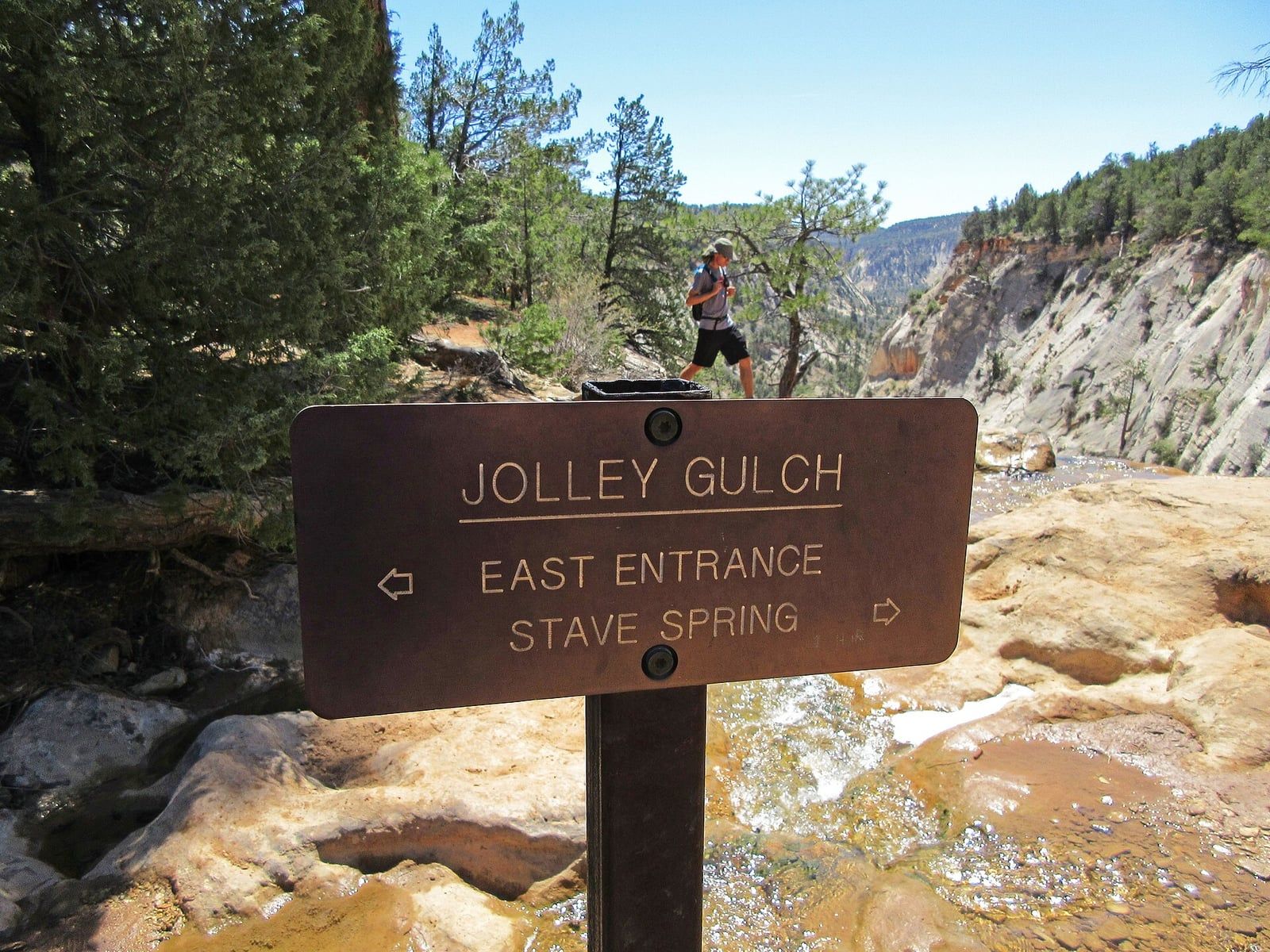 Jolley Gulch Trail Sign in Zion National Park A hiker passes the Jolley Gulch trail sign near a shallow creek in Zion National Park, Utah.