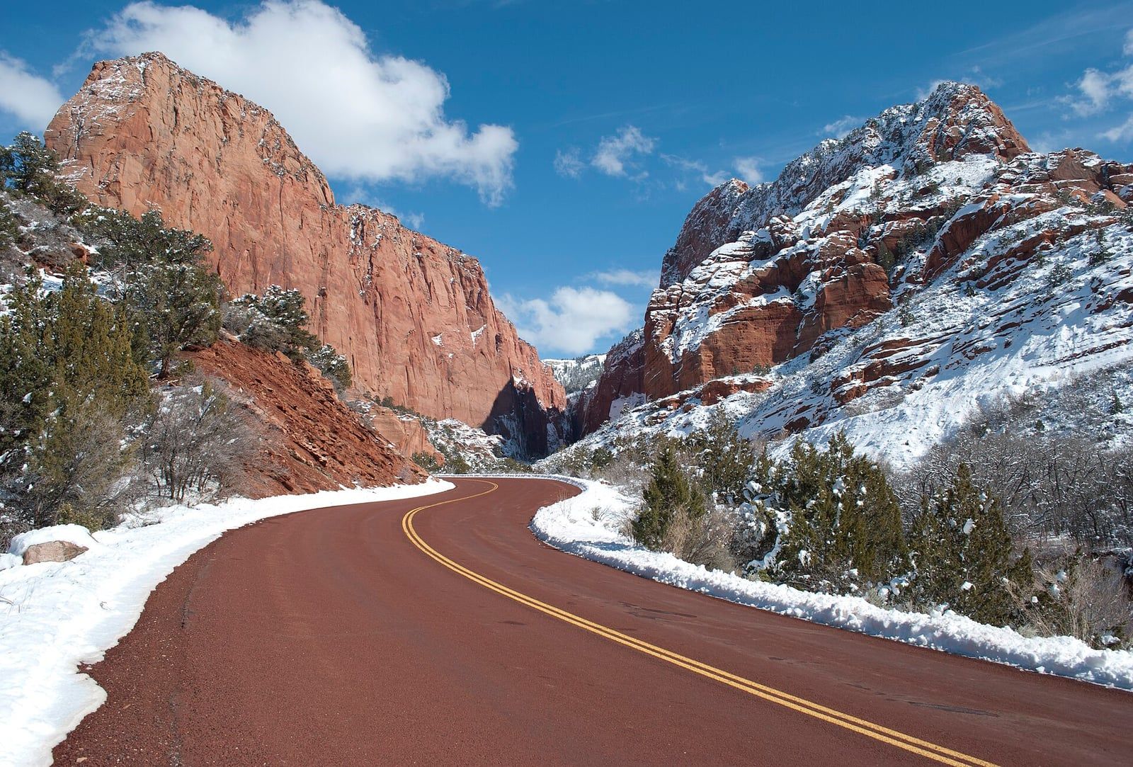 Kolob Canyon Scenic Drive in Winter A snow-lined road curves through Kolob Canyon's towering red sandstone cliffs under a bright winter sky.