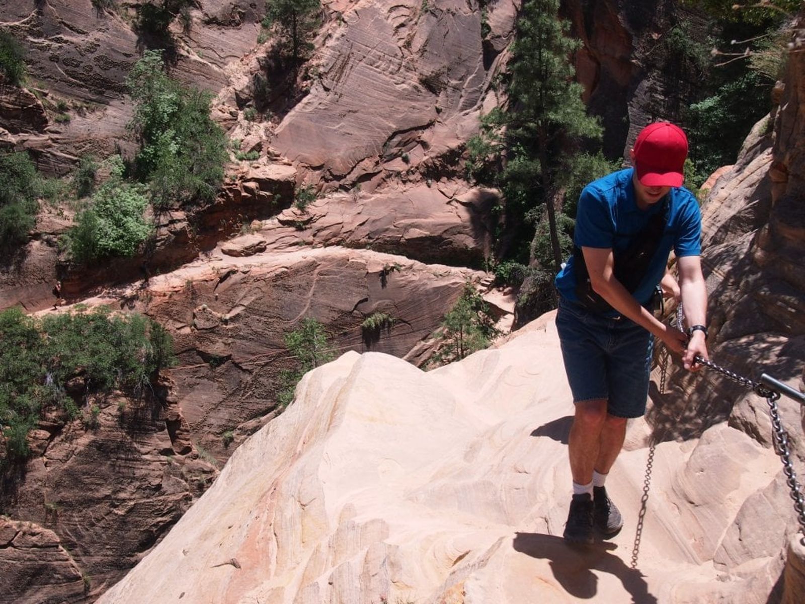 Hiker on Hidden Canyon Trail Chain Section, Zion A hiker grips the safety chains while navigating the steep sandstone ledge on Hidden Canyon Trail in Zion National Park.