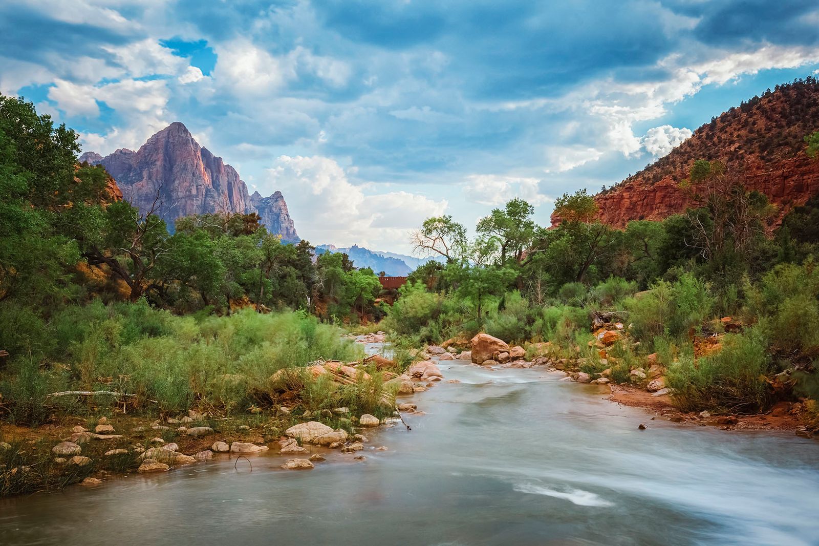 Virgin River flows through Zion Canyon beneath the Watchman peak with dramatic storm clouds and lush riverside vegetation