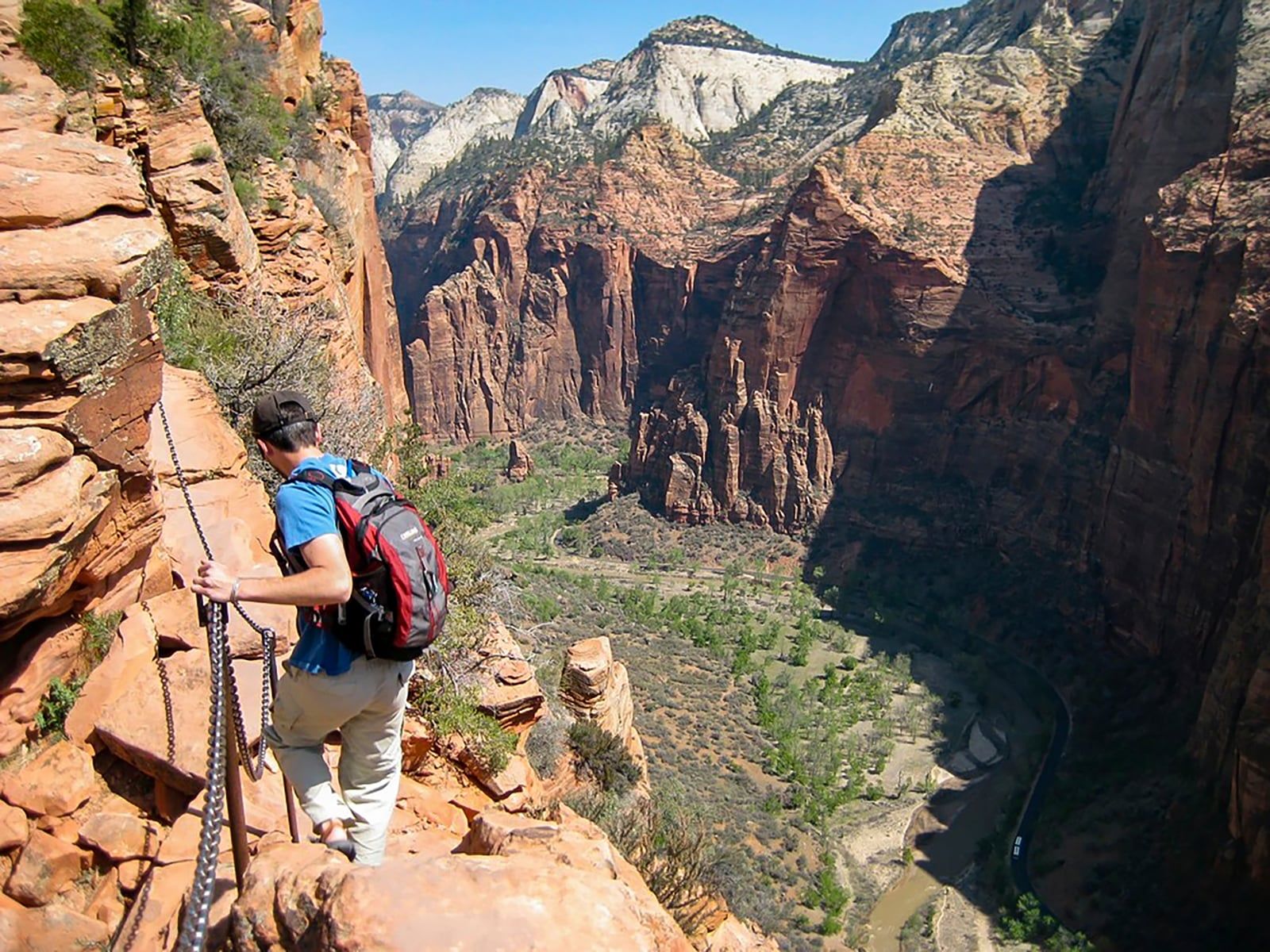 Hiker on Angels Landing Chain Section, Zion National Park A hiker grips the safety chain on Angels Landing trail, overlooking the dramatic red rock walls of Zion Canyon below.