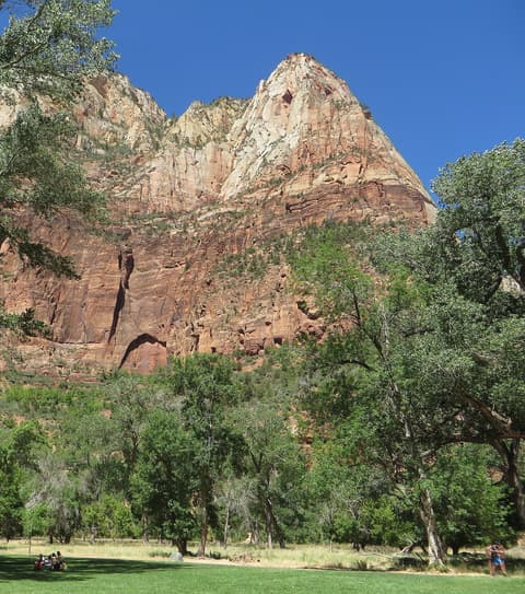 Visitors relax on the green lawn near Zion Lodge with towering Lady Mountain sandstone cliffs rising above the canyon.