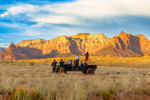 Tourists on private jeep tour photographing sunset illuminated red rock cliffs during Zion National Park adventures and scenic overlook experiences