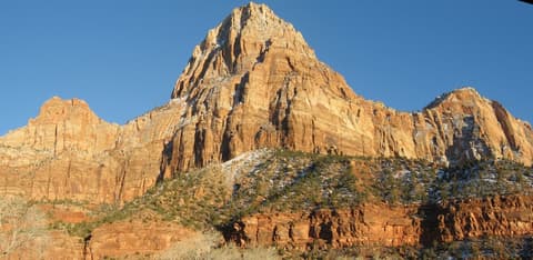Bridge Mountain rises above snow-dusted sandstone cliffs and evergreens in Zion National Park, Utah.