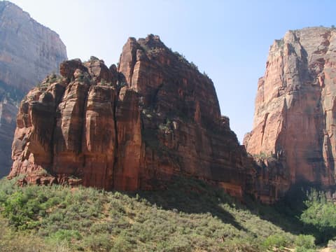 Massive red sandstone monolith known as The Organ rising above Zion Canyon shrubland beneath a clear blue sky.