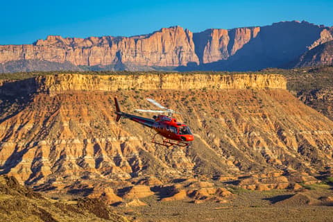 Red helicopter flying over dramatic sandstone cliffs and canyons during a scenic Zion National Park tour in southern Utah