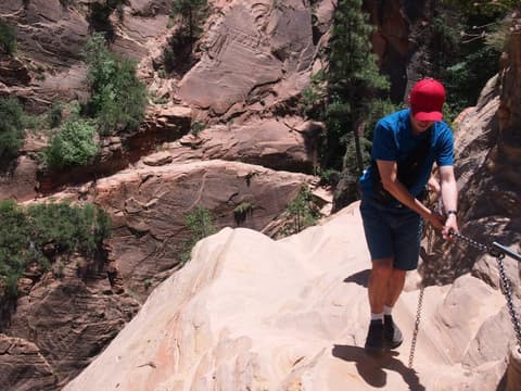 A hiker grips the safety chains while navigating the steep sandstone ledge on Hidden Canyon Trail in Zion National Park.