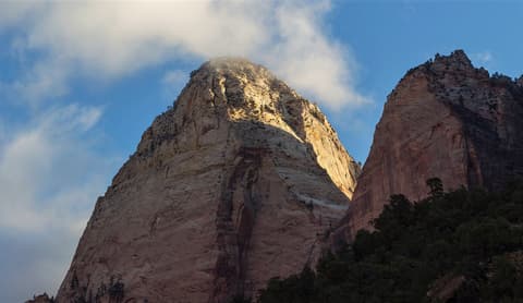 Sunlit sandstone summit of Mountain of the Sun rising above Zion Canyon with dramatic clouds in southern Utah.