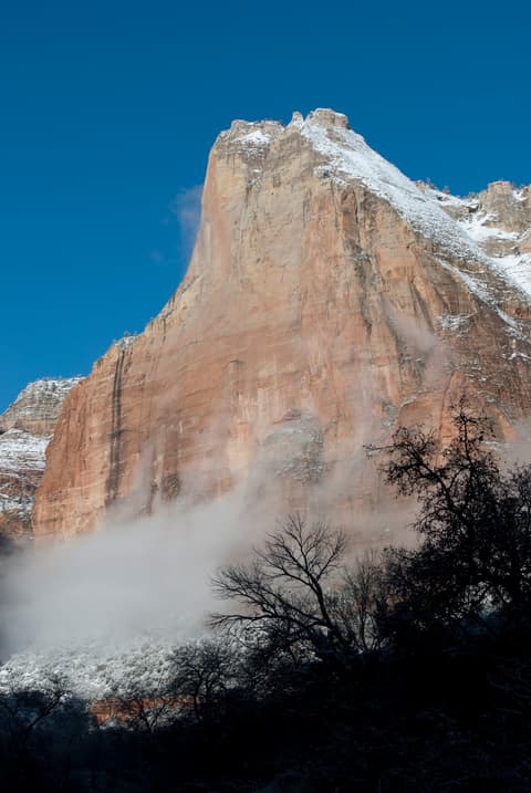 Snow-dusted Abraham Peak rises above winter mist and bare trees in Zion National Park, Utah.