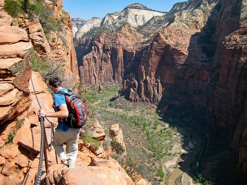 A hiker grips the safety chain on Angels Landing trail, overlooking the dramatic red rock walls of Zion Canyon below.