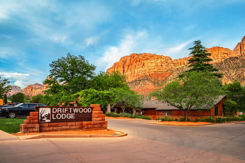 Driftwood Lodge entrance sign with stunning red rock canyon cliffs backdrop in Springdale offering hotels near Zion National Park Utah lodging accommodations