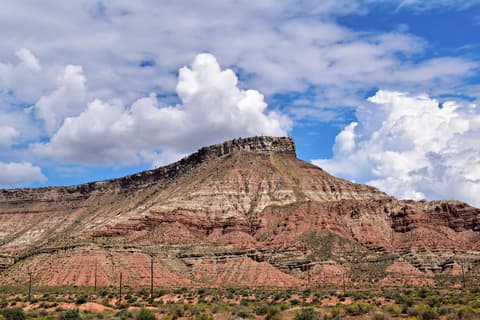 A flat-topped red rock mesa with layered sandstone rises above desert scrubland near Zion National Park, Utah.