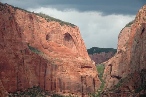 A massive blind arch carved into red sandstone cliffs in Kolob Canyon, Zion National Park, under stormy skies.