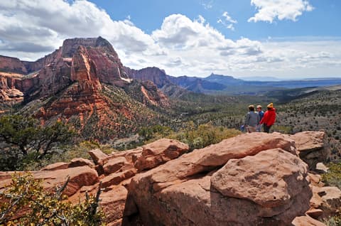 Three hikers stand on a red sandstone overlook taking in the sweeping panoramic views of Kolob Canyon in Zion National Park.