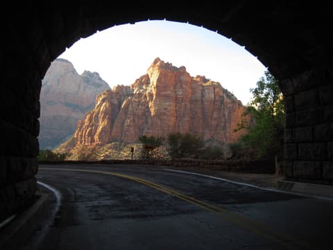 View of Zion's red rock cliffs framed by a tunnel entrance with a clear blue sky.