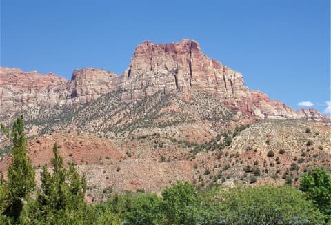 A massive red sandstone butte rises above scrub trees and desert slopes in Zion Canyon, Utah.