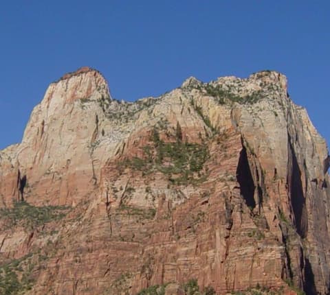 The Sentinel's towering sandstone cliffs rise dramatically above Zion Canyon under a clear blue sky.