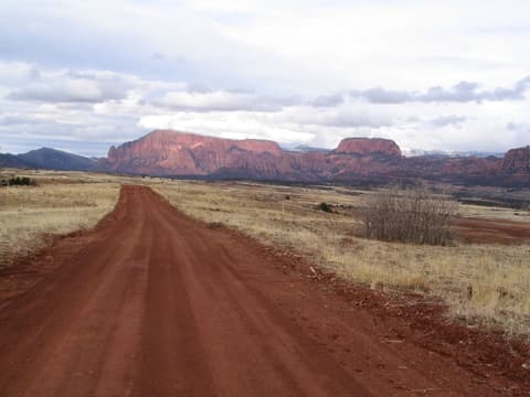 A red dirt road stretches toward dramatic red rock mesas near Kolob Canyon in Zion National Park, Utah.