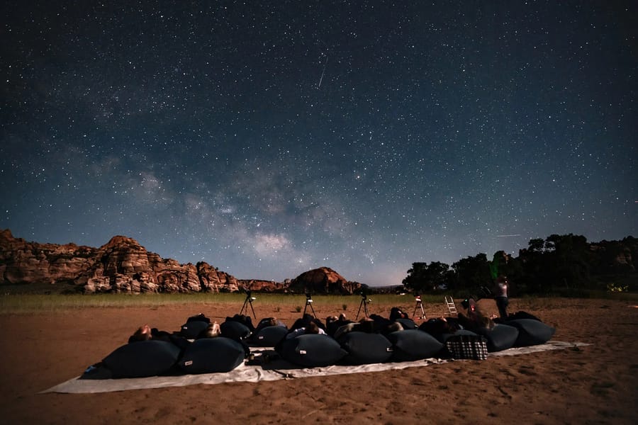 A group of people stargazing under a clear night sky with the Milky Way visible, in a desert landscape near Zion National Park.